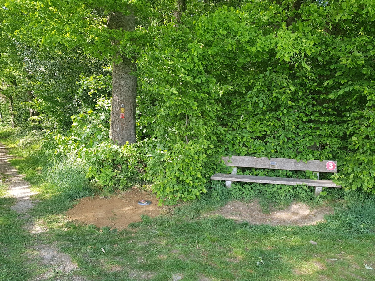 Bank an einem Wanderweg, daneben ein Erdloch.