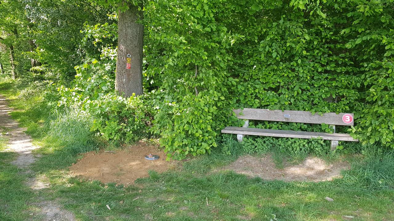 Bank an einem Wanderweg, daneben ein Erdloch.