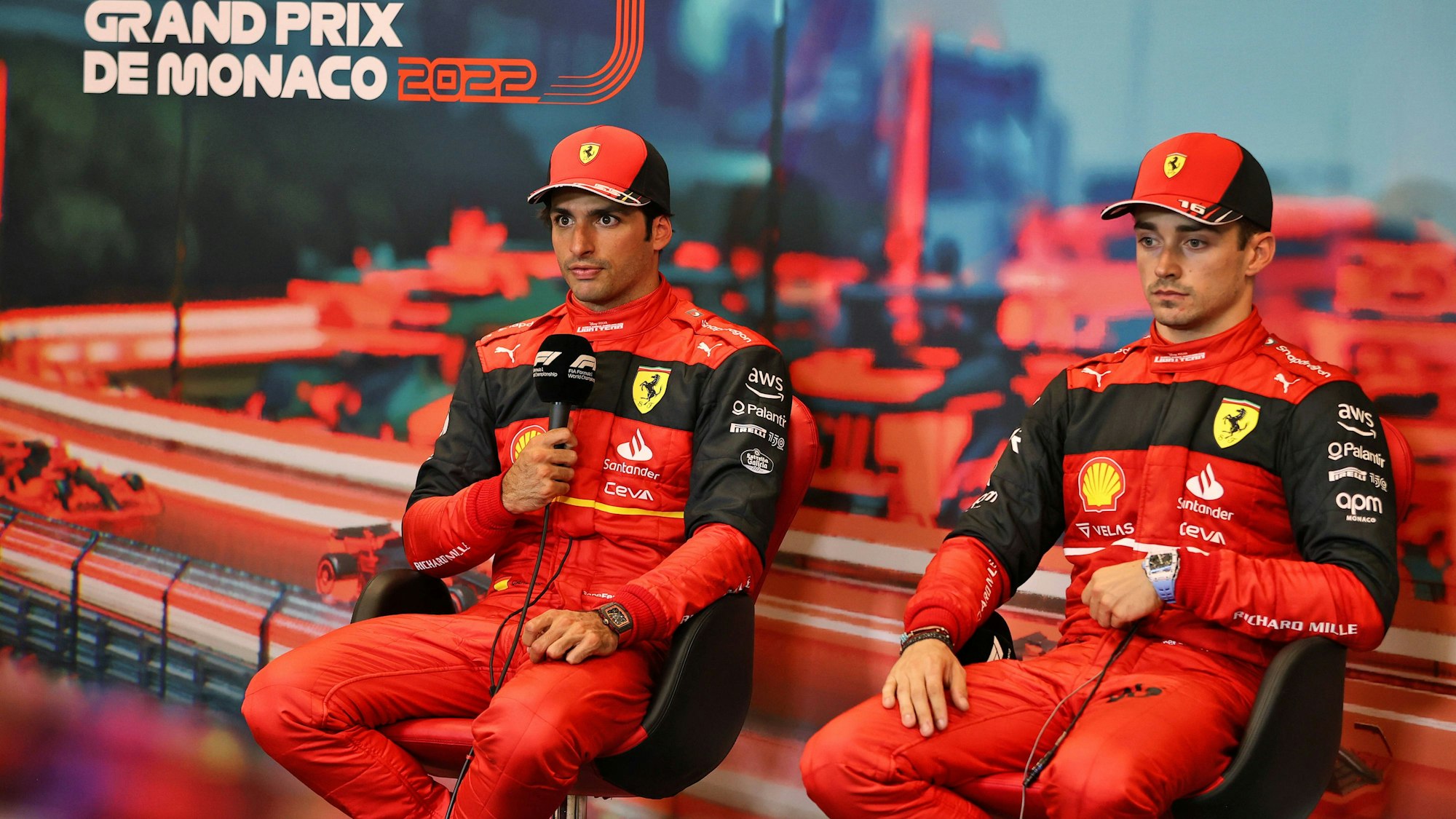 Carlos Sainz hält auf einer Pressekonferenz das Mikrofon in der Hand und spricht mit den Journalisten, daneben sein Teamkollege Charles Leclerc.