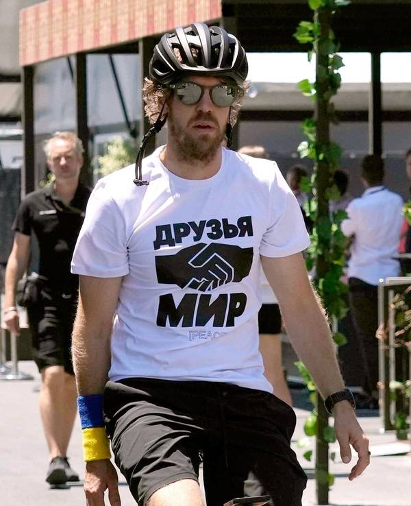 Sebastian Vettel, vom Team Aston Martin, kommt auf einem Fahrrad zum dritten freien Training. Er trägt ein weißes T-Shirt, auf dem die russischen Worte „Freunde“ und „Frieden“ stehen und zwei Hände beim Handschlag abgebildet sind.