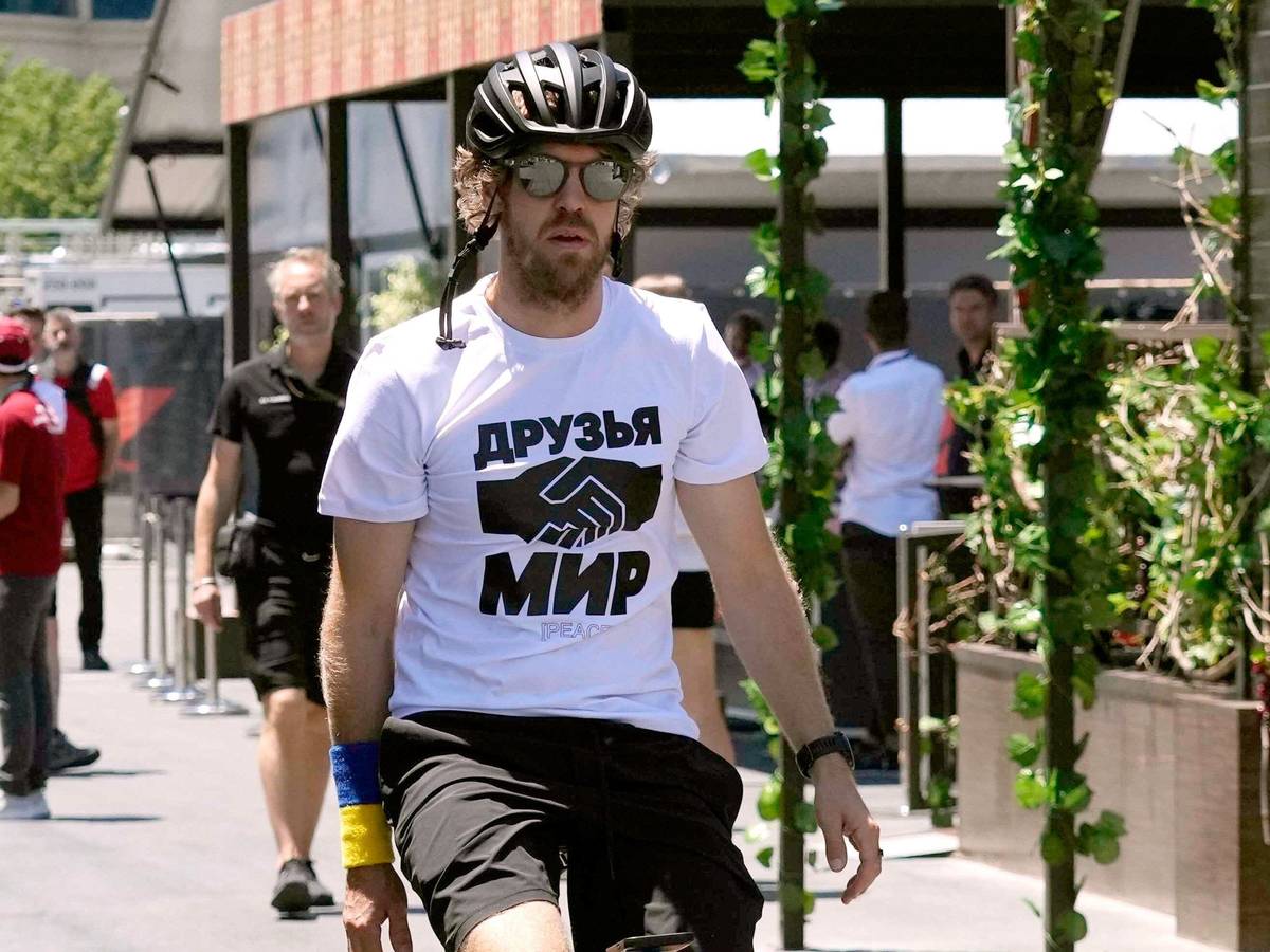 Sebastian Vettel, vom Team Aston Martin, kommt auf einem Fahrrad zum dritten freien Training. Er trägt ein weißes T-Shirt, auf dem die russischen Worte „Freunde“ und „Frieden“ stehen und zwei Hände beim Handschlag abgebildet sind.