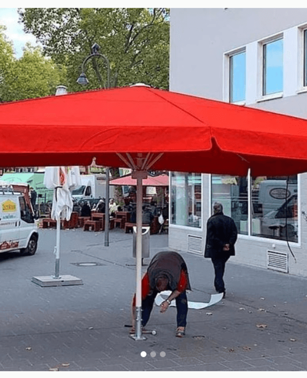 Ein Mann stellt einen großen roten Schirm auf dem Chlodwigplatz auf.