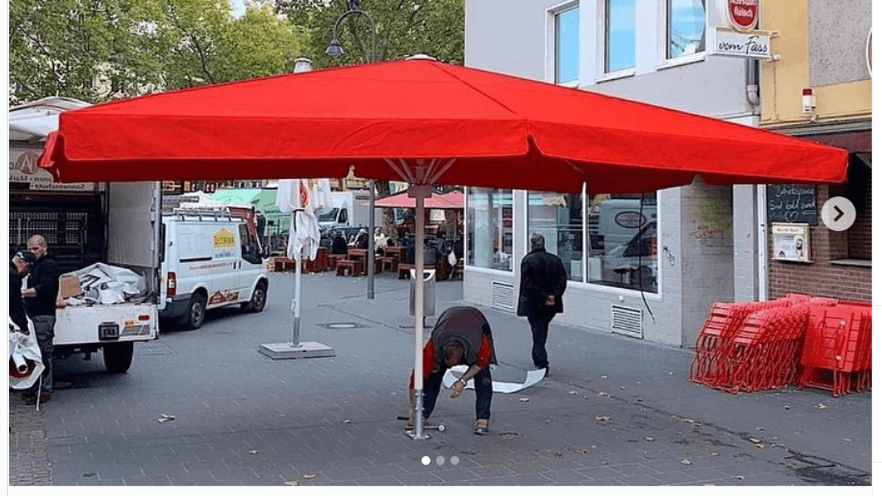 Ein Mann stellt einen großen roten Schirm auf dem Chlodwigplatz auf.