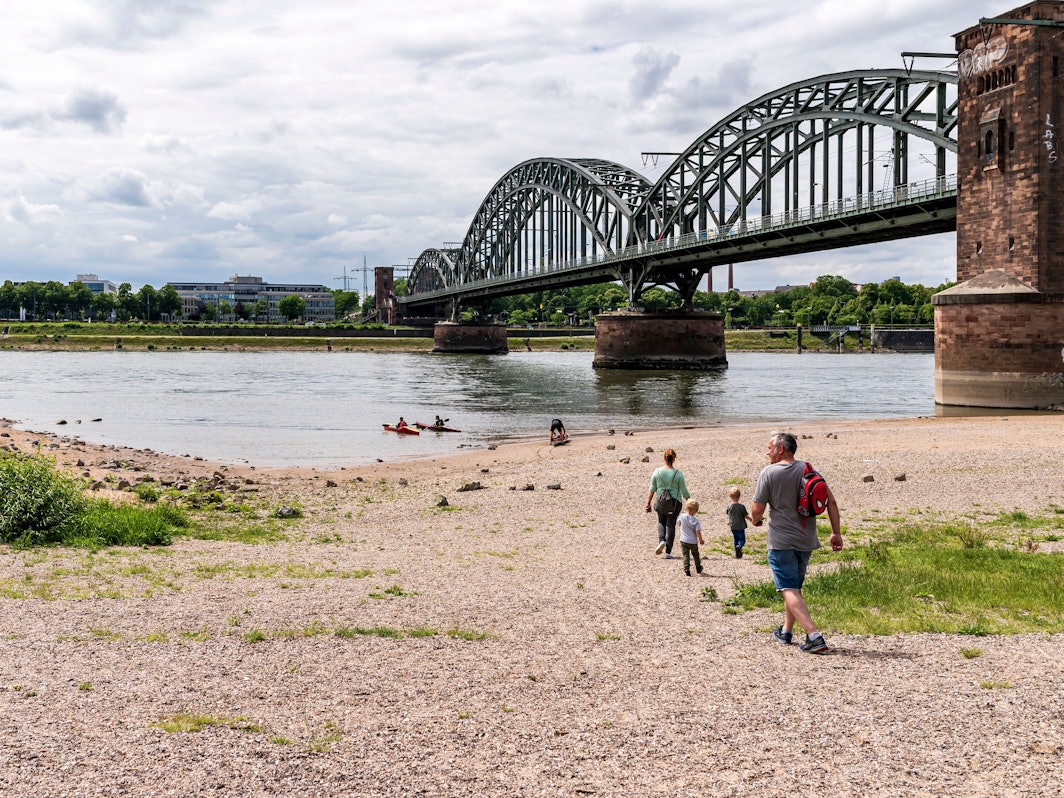 Menschen gehen am Rhein spazieren, die Sonne scheint.