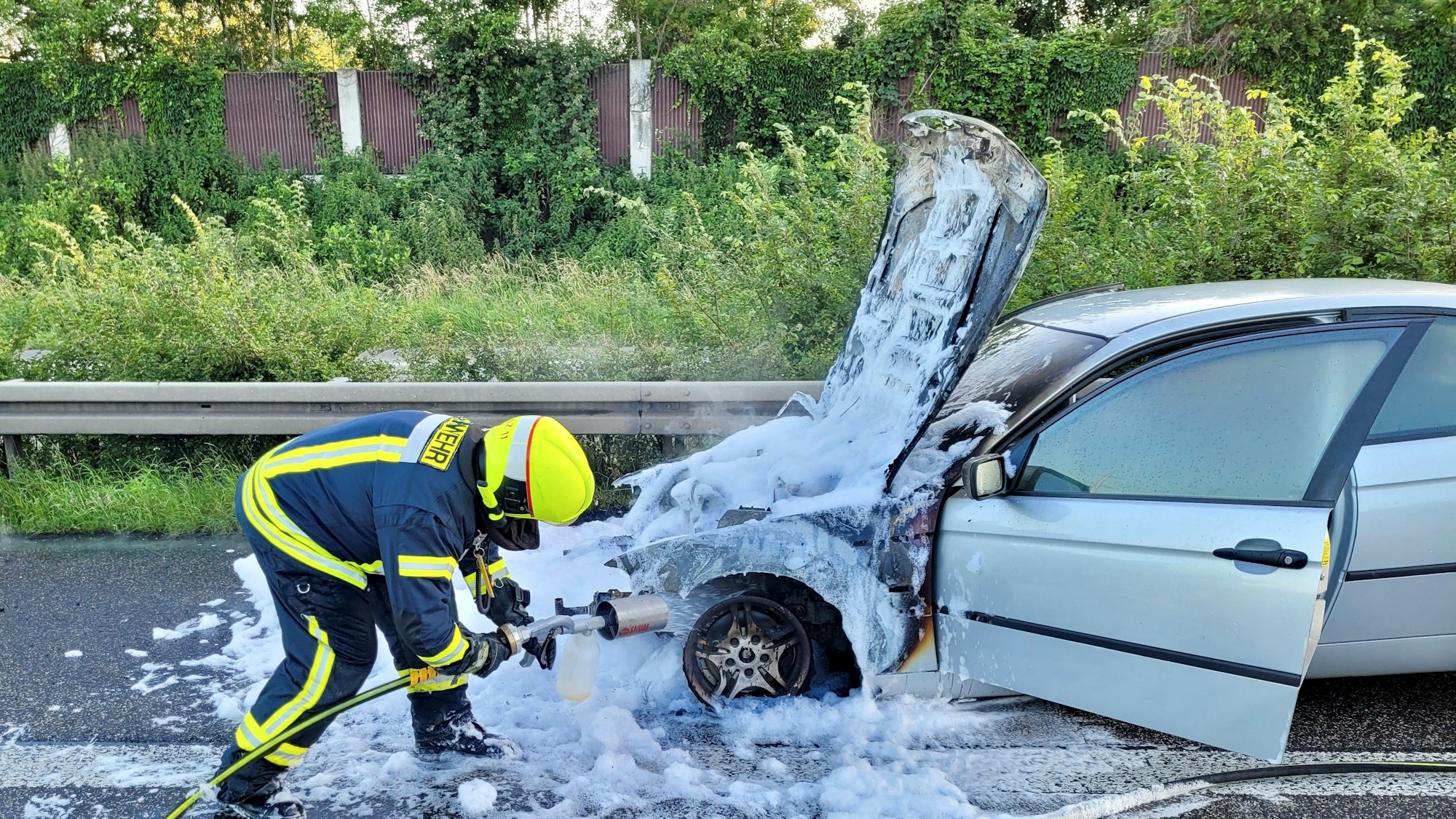 Ein Feuerwehrmann besprüht den Unfallwagen mit Löschschaum.