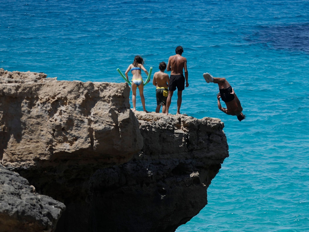 Menschen springen am Felsenstrand von Maioris an der Südostküste Mallorcas ins Meer.