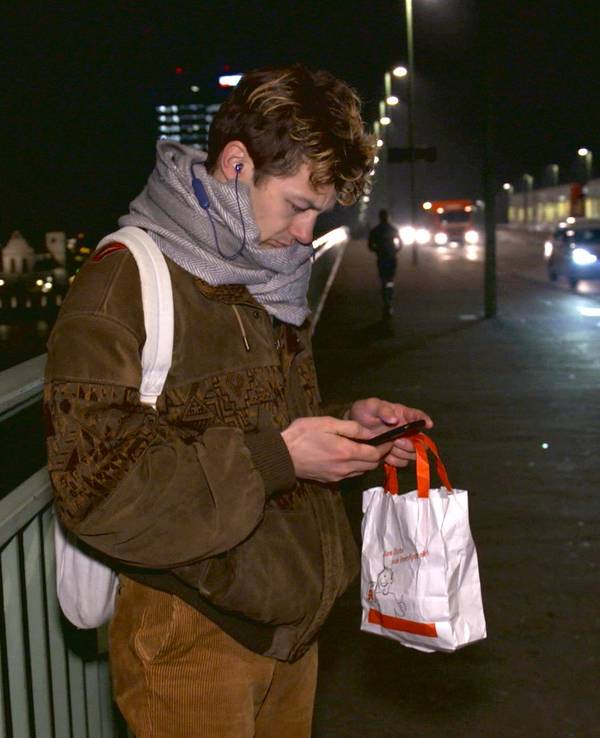 Schauspieler Tim-Fabian Hoffmann steht Nachts auf der Deutzer Brücke und schaut auf sein Handy.