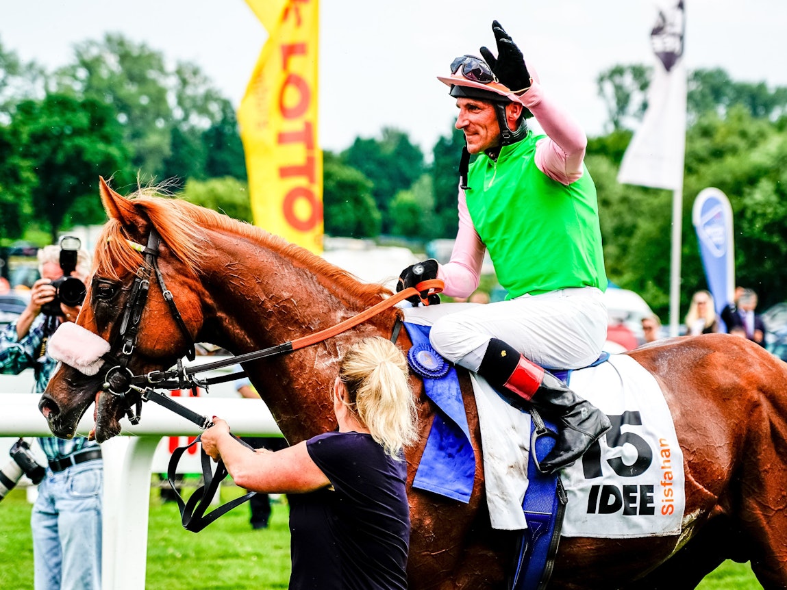 Jockey Andrasch Starke sitzt auf seinem Pferd und winkt.