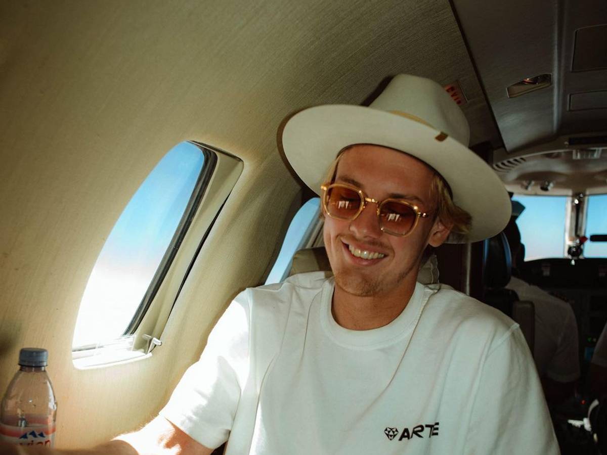 Julian Brandt sitzt mit Hut in einem Privatjet.