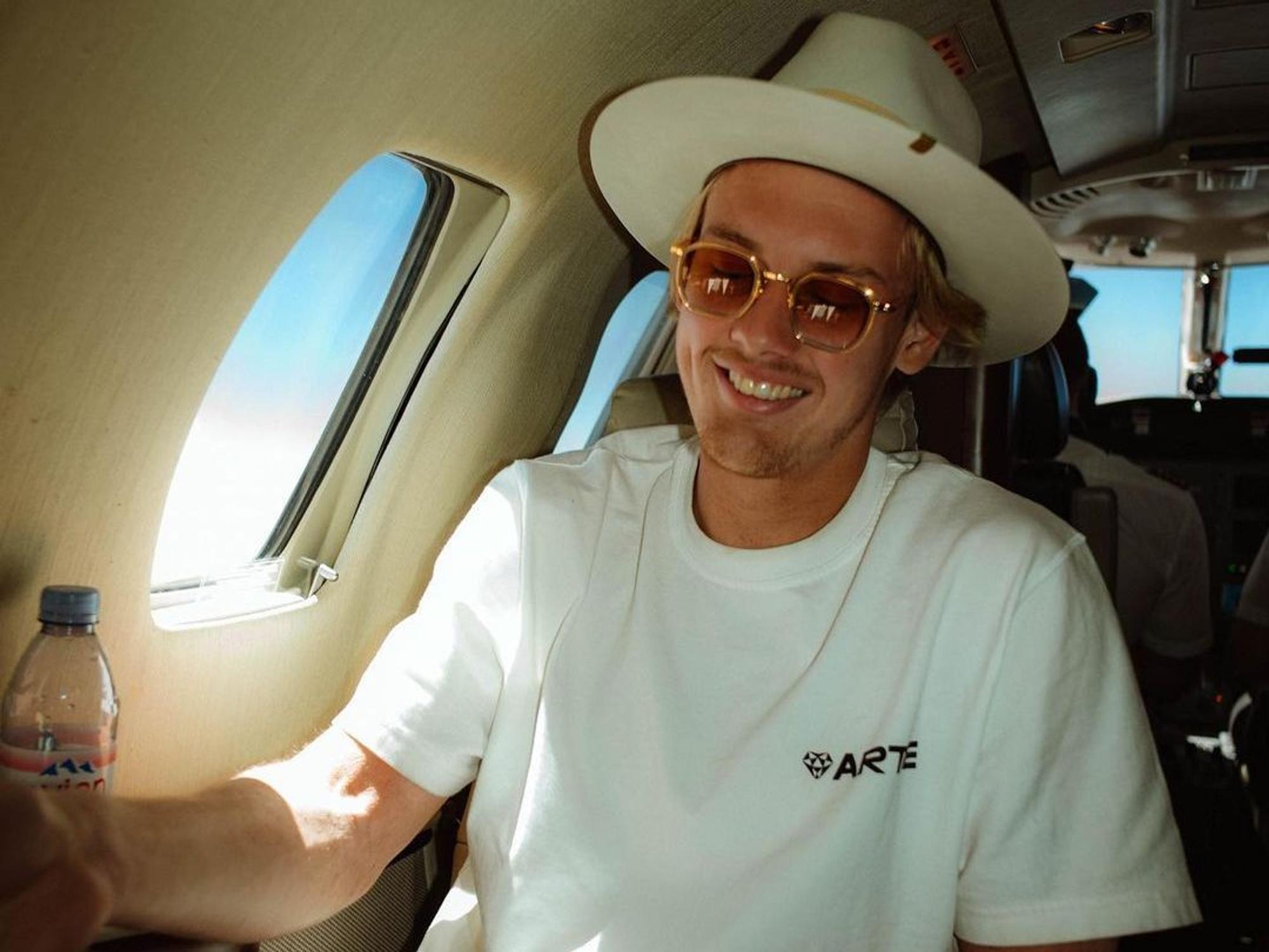 Julian Brandt sitzt mit Hut in einem Privatjet.