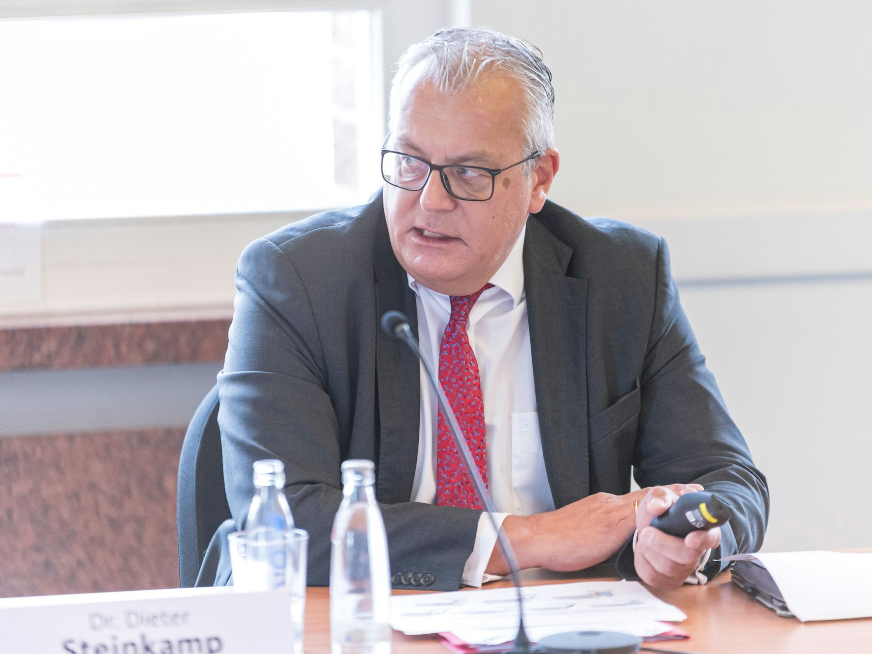 Dr. Dieter Steinkamp sitzt bei einer Pressekonferenz vor einem Mikrofon.