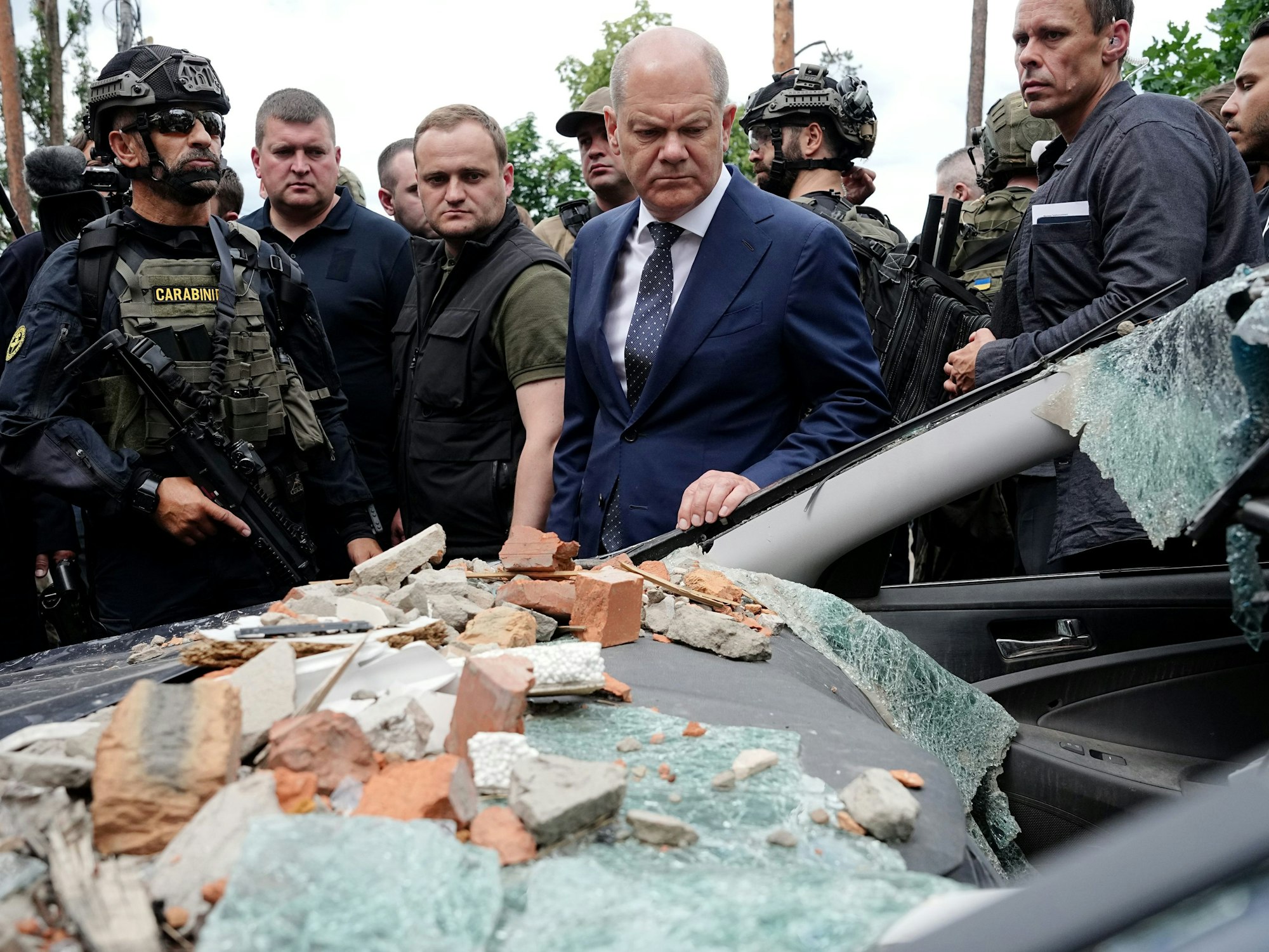 Bundeskanzler Olaf Scholz (M, SPD) blickt bei seinem Besuch auf ein stark beschädigtes Auto in Irpin im Großraum Kyjiw.