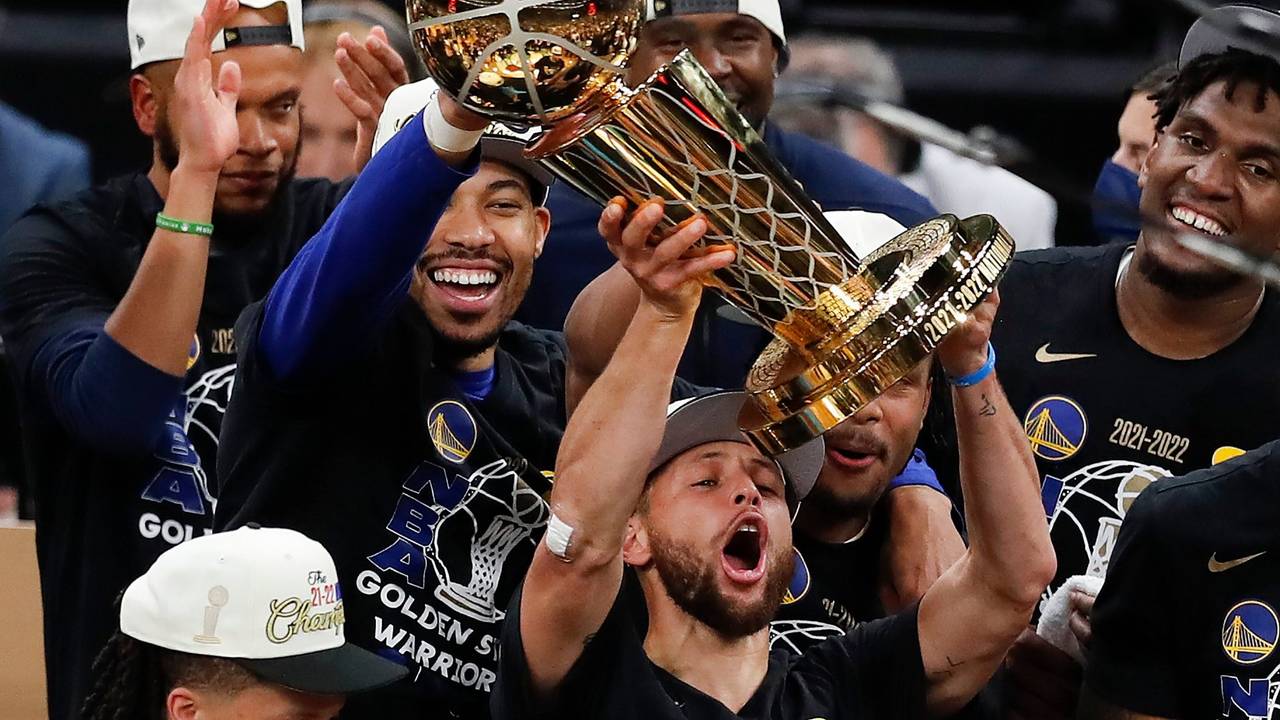 Stephen Curry stemmt vor seinen feiernden Kollegen die NBA-Trophäe in die Luft.