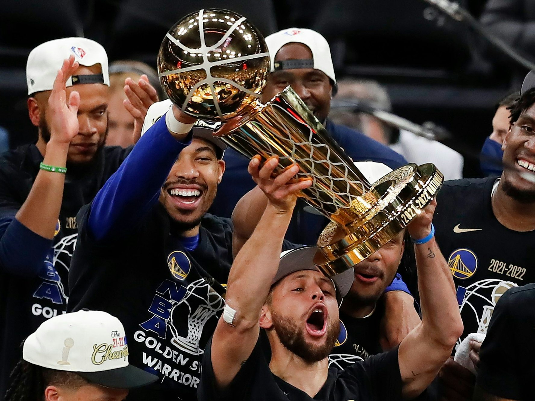 Stephen Curry stemmt vor seinen feiernden Kollegen die NBA-Trophäe in die Luft.
