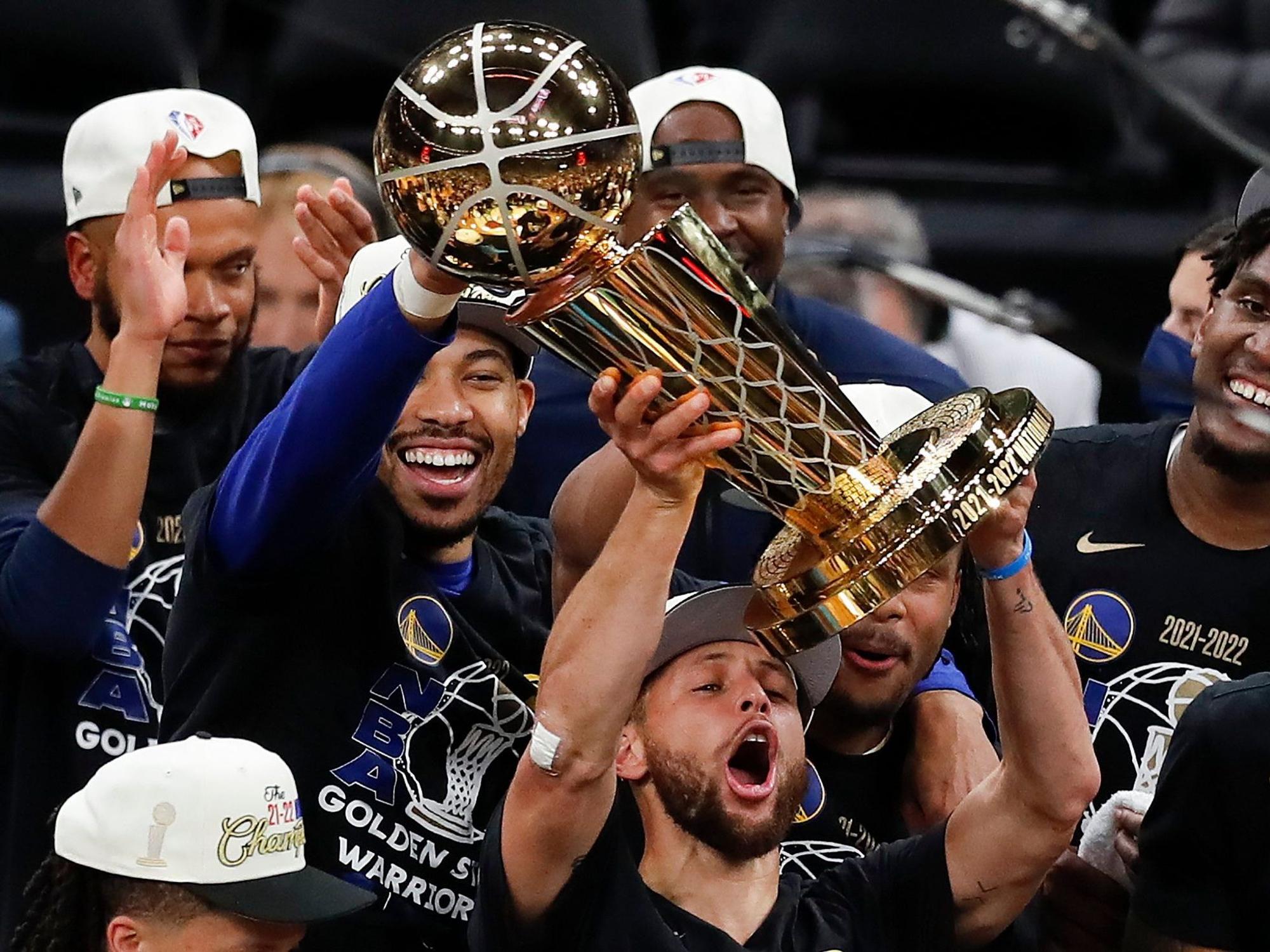 Stephen Curry stemmt vor seinen feiernden Kollegen die NBA-Trophäe in die Luft.