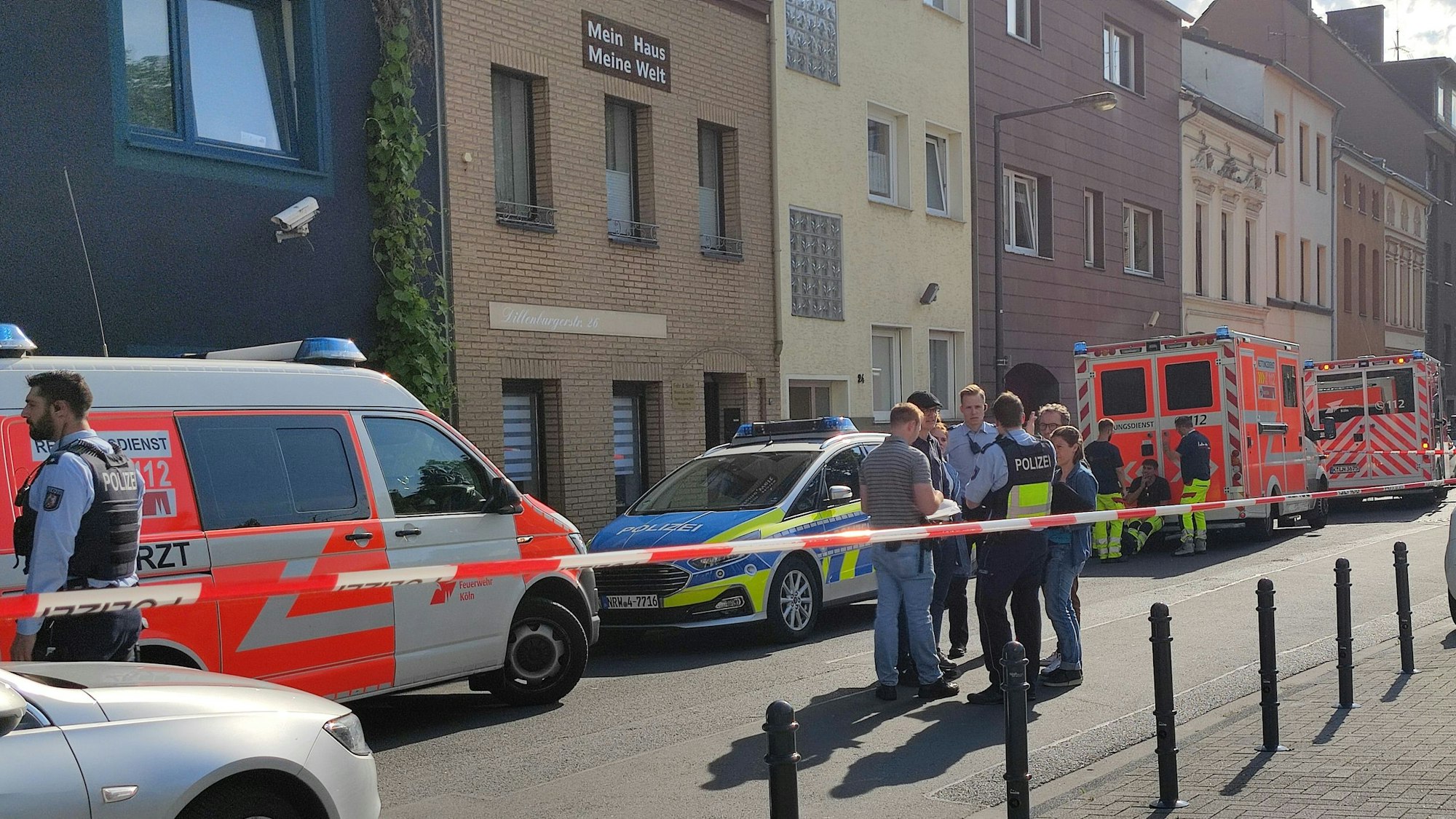 Einsatzkräfte der Polizei sowie ein Streifenwagen und mehrere Fahrzeuge des Rettungsdienstes stehen vor dem Haus, in dem das Tötungsdelikt passierte.