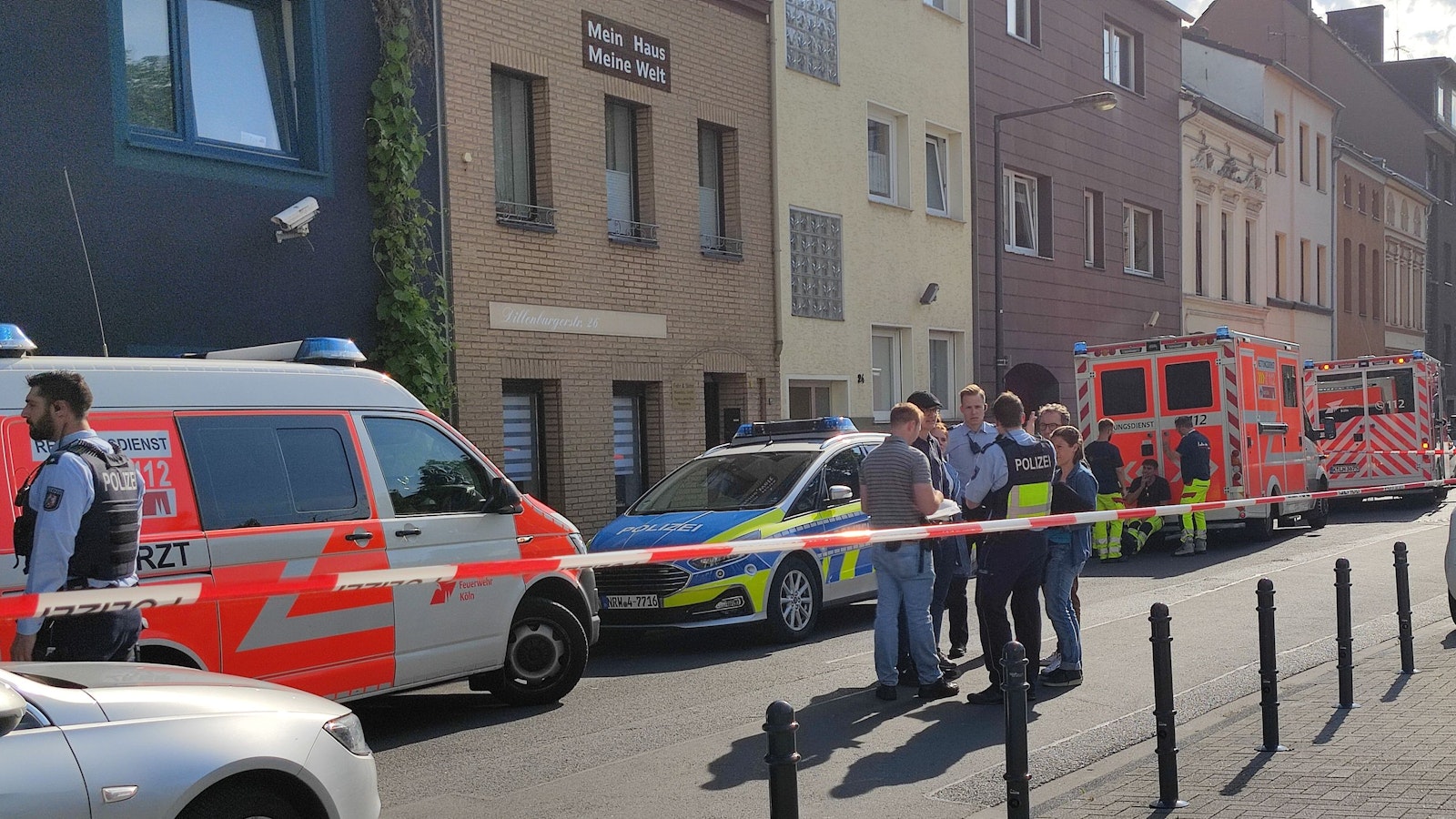 Einsatzkräfte der Polizei sowie ein Streifenwagen und mehrere Fahrzeuge des Rettungsdienstes stehen vor dem Haus, in dem das Tötungsdelikt passierte.