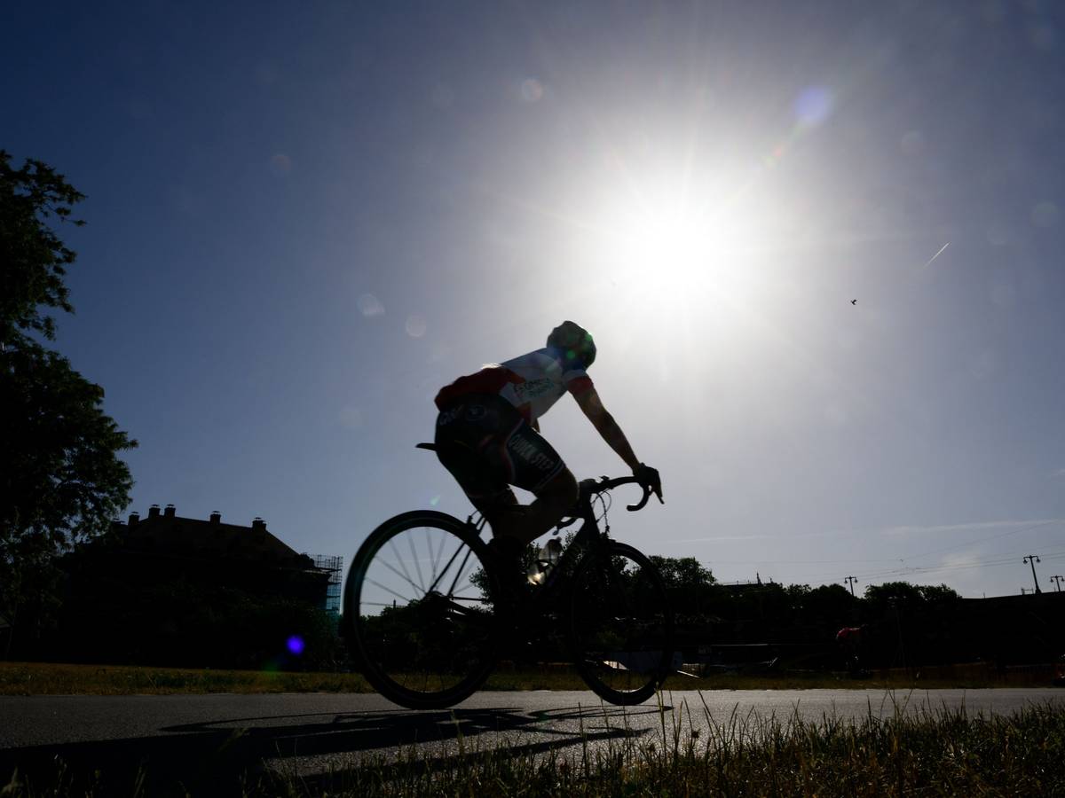 Ein Rennradfahrer fährt am Morgen auf dem Elberadweg am Blockhaus entlang während am Himmel die Sonne scheint.