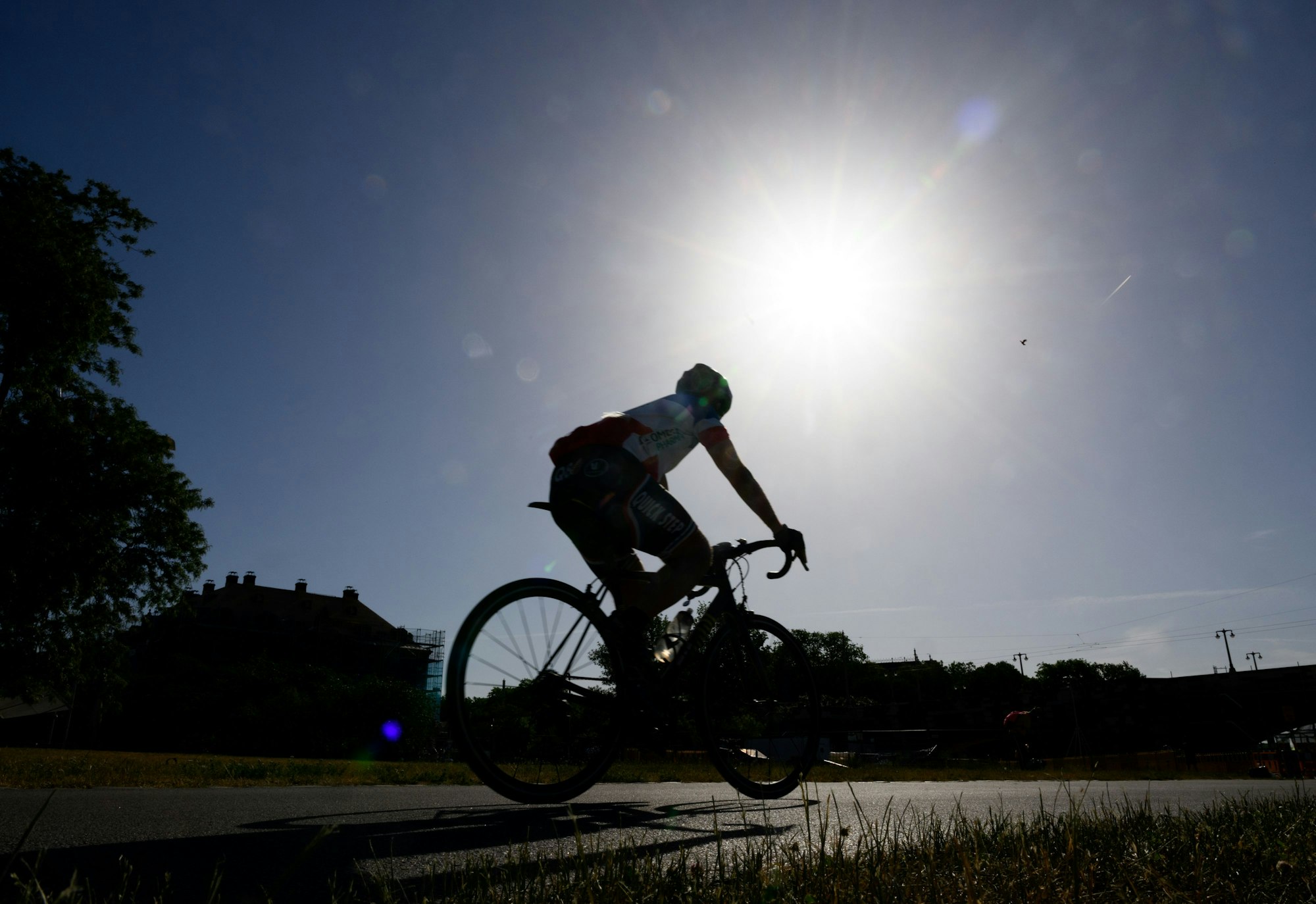 Ein Rennradfahrer fährt am Morgen auf dem Elberadweg am Blockhaus entlang während am Himmel die Sonne scheint.