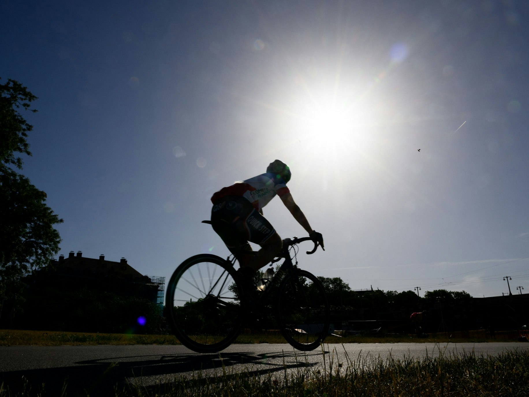 Ein Rennradfahrer fährt am Morgen auf dem Elberadweg am Blockhaus entlang, während am Himmel die Sonne scheint.