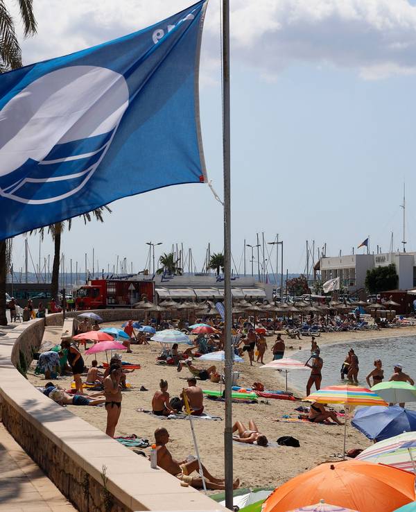 Eine blaue Flagge weht am Strand der Bucht Cala Estancia im Wind.