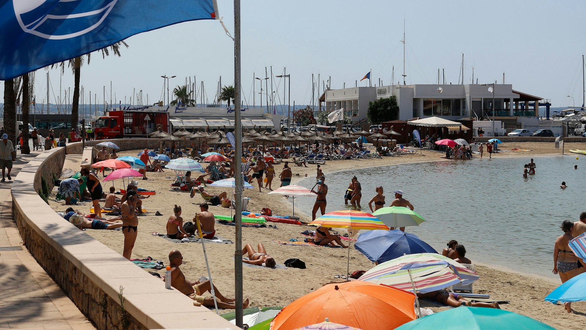 Eine blaue Flagge weht am Strand der Bucht Cala Estancia im Wind.