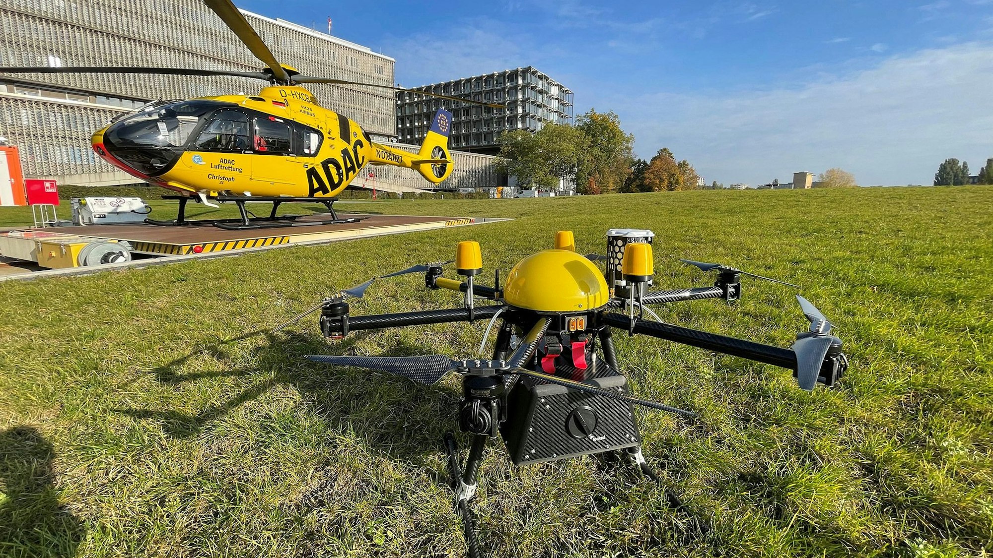 Die Transportdrohne, mit der rund 100 Forschungsflüge durchgeführt wurden, steht auf einer Rasenfläche an der Charite in Berlin (undatierte Aufnahme). Im Hintergrund ist der ADAC Rettungshubschrauber „Christoph 31“ zu sehen. In Ulm wird bislang erfolgreich an der eiligen Blutspende aus der Luft geprobt.
