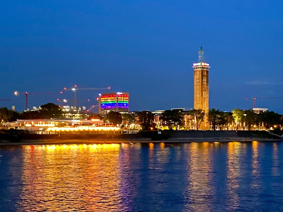 Ein Blick auf Köln-Deutz in der Dunkelheit. Ein Gebäude zeigt sich in Regenbogenfarben.