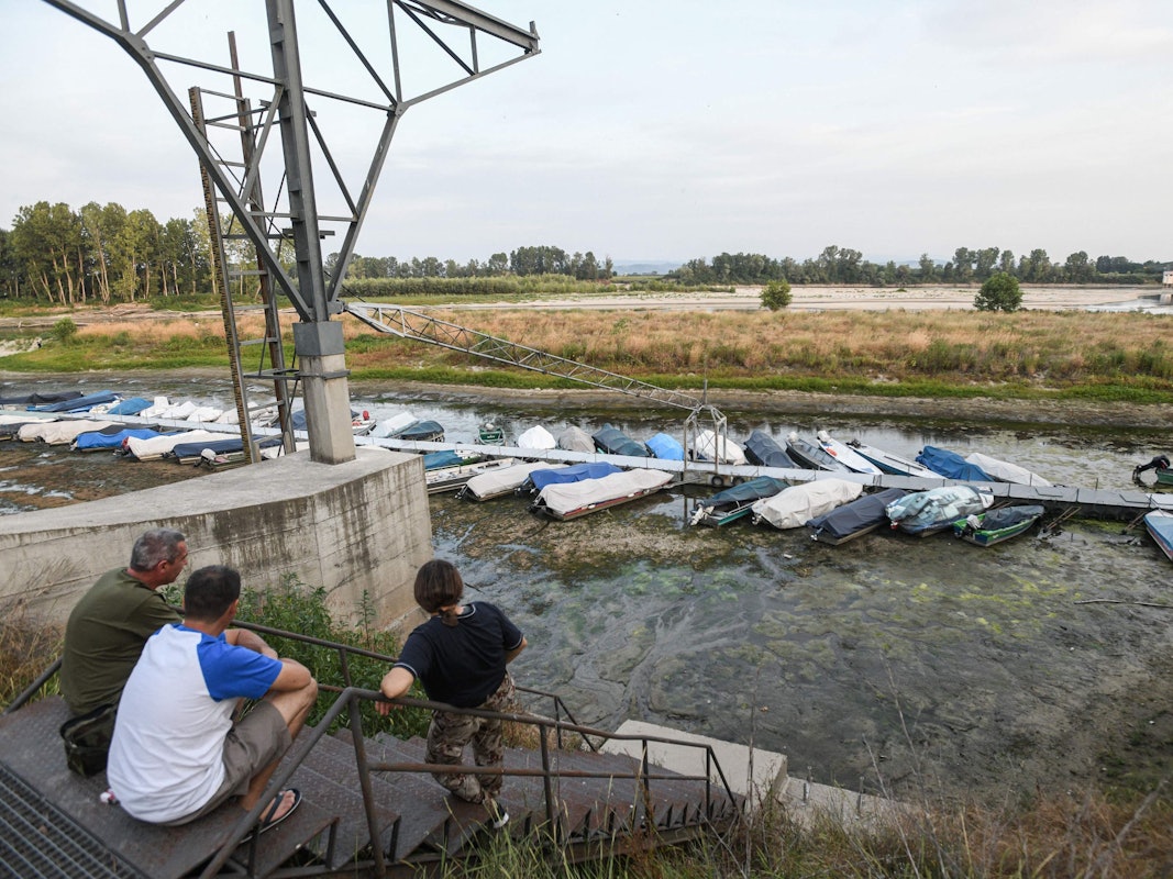 Menschen sitzen bei Ponte della Becca, in der Nähe von Linarolon in der Provinz Pavia in der Lombardei, am 17. Juni 2022 und blicken auf Boote, die bei Niedrigwasser festgemacht sind. In der Region herrscht seit vielen Tagen Dürre und Trockenheit.