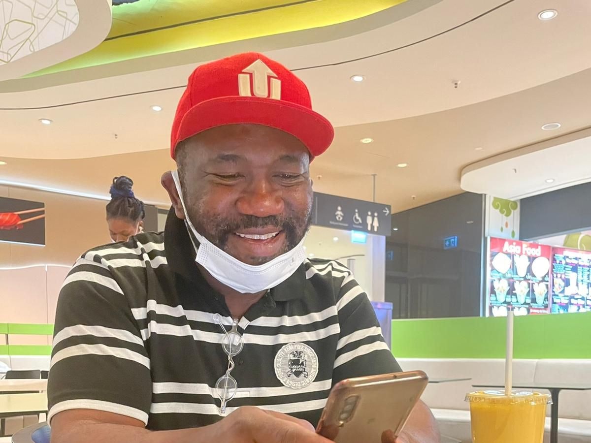 Joseph René Samnick (55) sitzt mit Handy an einem Tisch. Er wurde in einem Obdachlosenheim in Köln massiv rassistisch beleidigt.