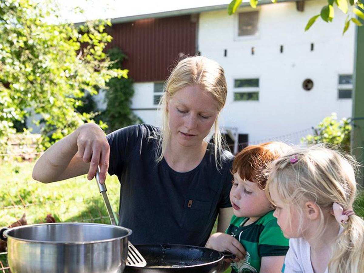 Zwei Kinder bereiten mit Landwirtin Carolin Lawnik Kräuterpfannkuchen zu.