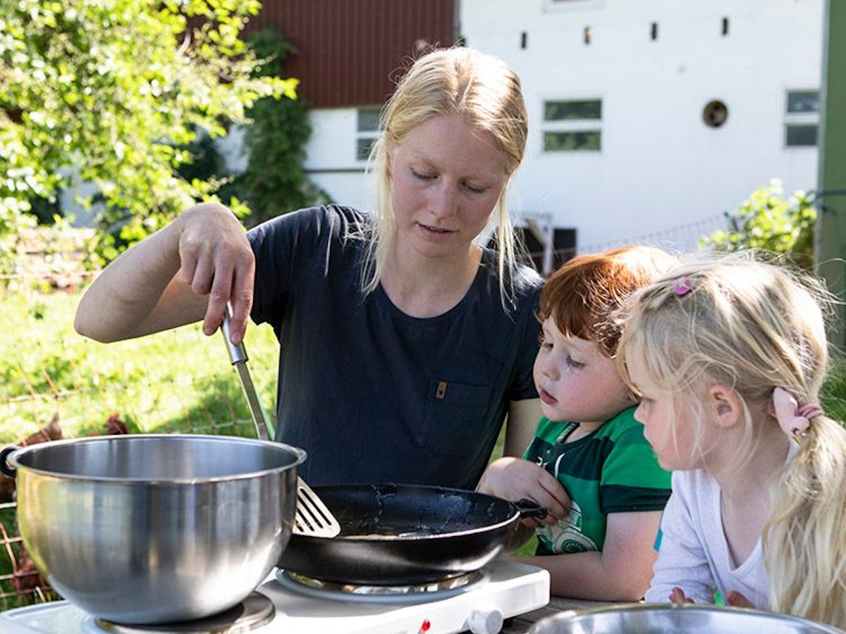 Zwei Kinder bereiten mit Landwirtin Carolin Lawnik Kräuterpfannkuchen zu.