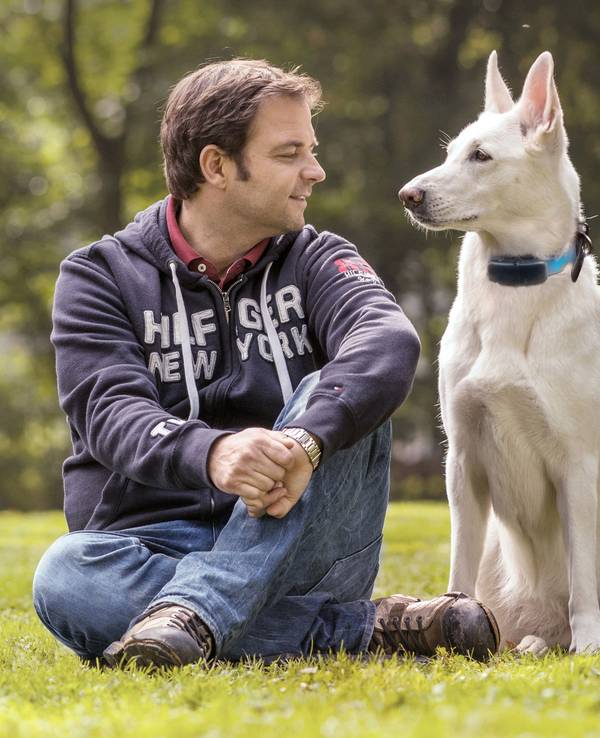 Das Foto zeigt Hundetrainer Martin Rütter sitzend auf einer Wiese mit einem Hund.