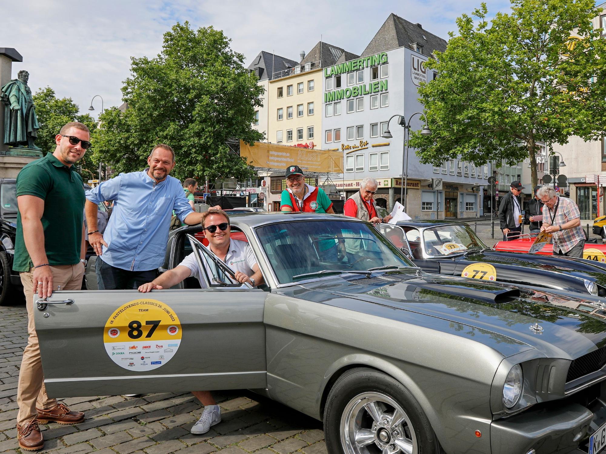 Vier Männer posieren mit einem Oldtimer.