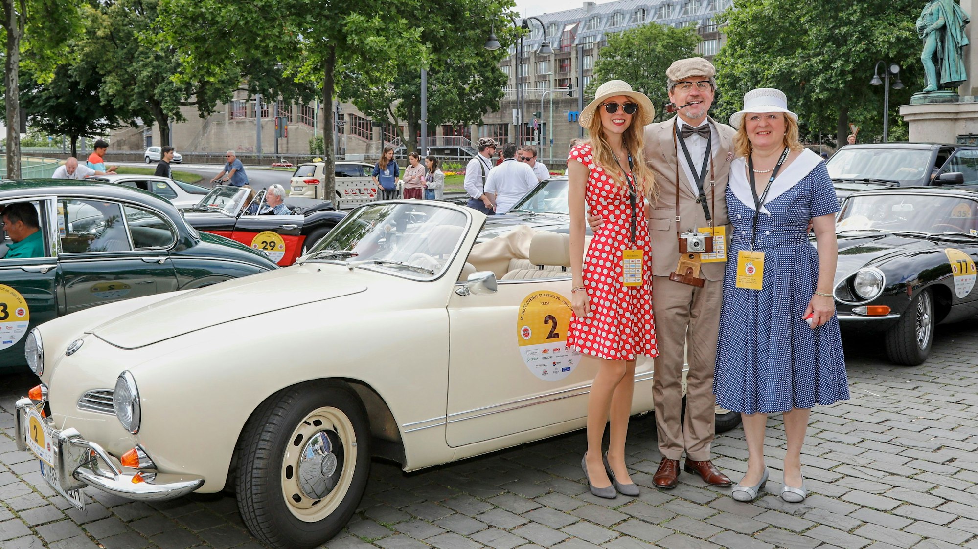 Ein Mann und zwei Frauen vor einem Oldtimer.