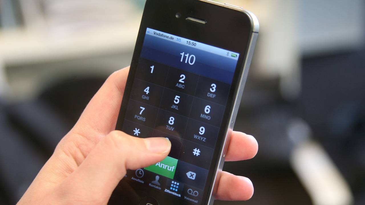 Eine junge Frau hält ein Smartphone mit der eingegebenen Notrufnummer 110 in der Hand.