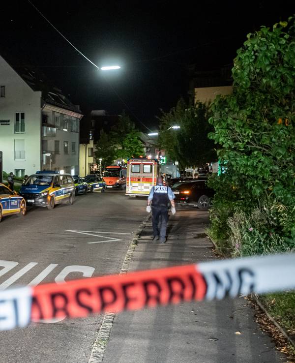 Polizeiautos stehen auf einer Straße hinter Absperrband.