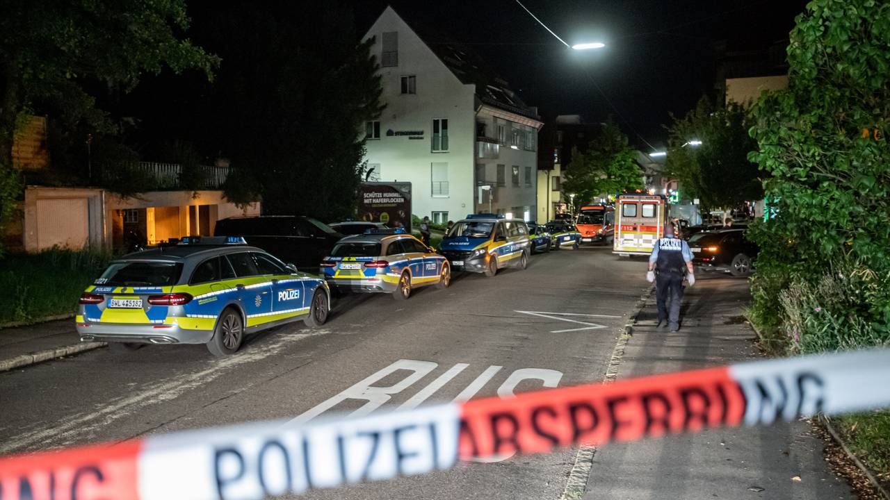 Polizeiautos stehen auf einer Straße hinter Absperrband.
