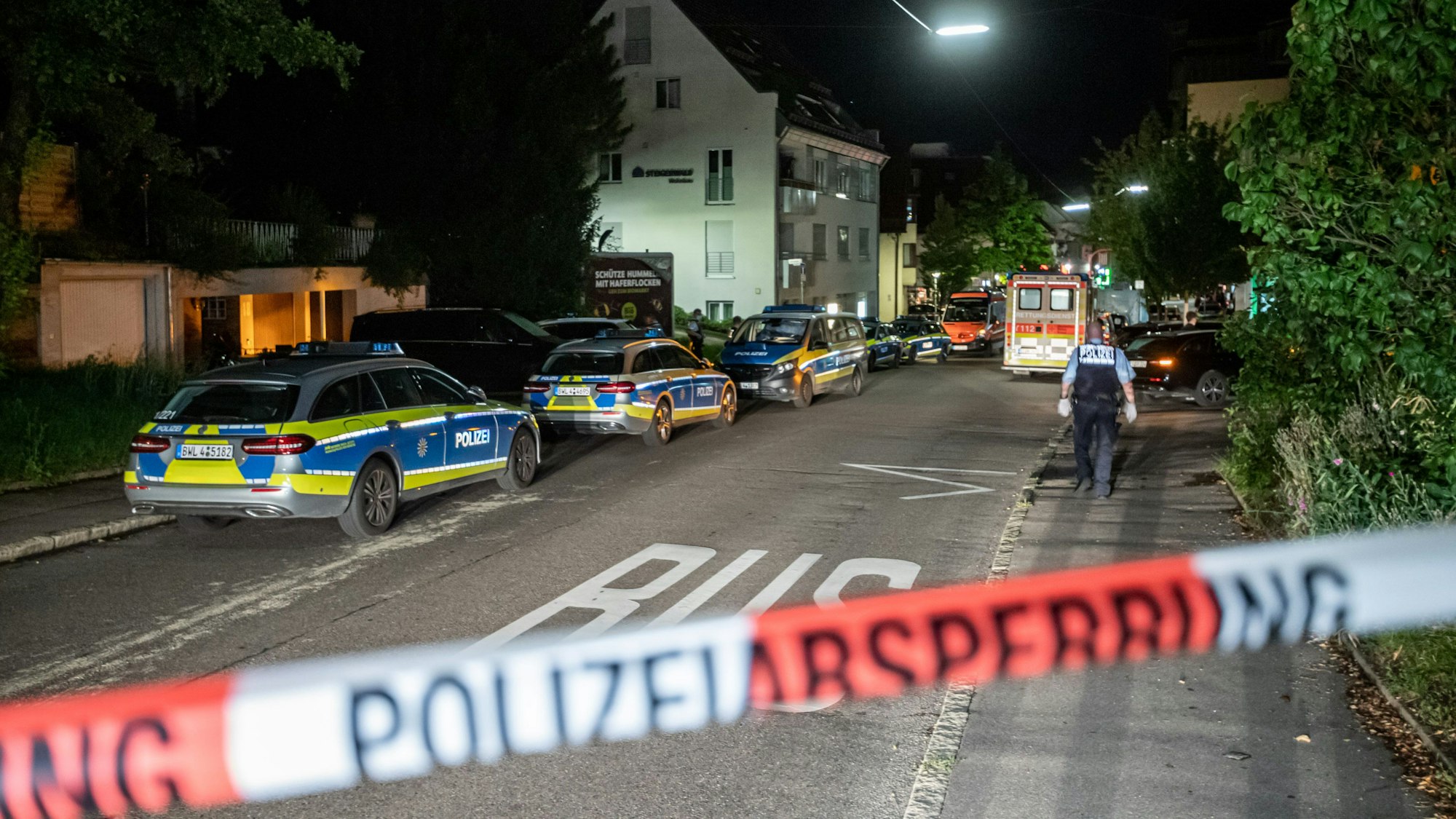 Polizeiautos stehen auf einer Straße hinter Absperrband.