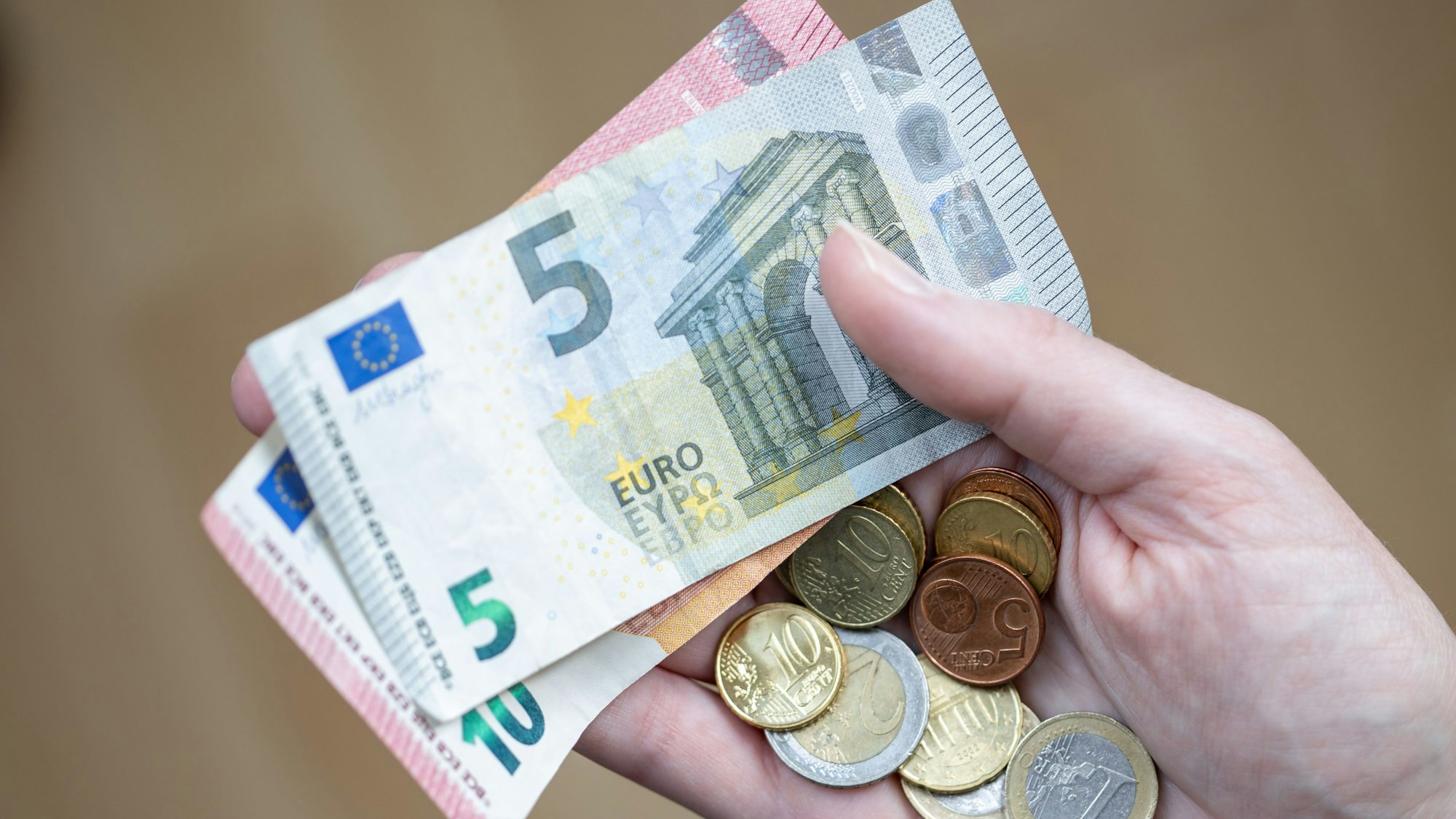 Eine Frau hält Geldscheine und Münzen in der Hand.