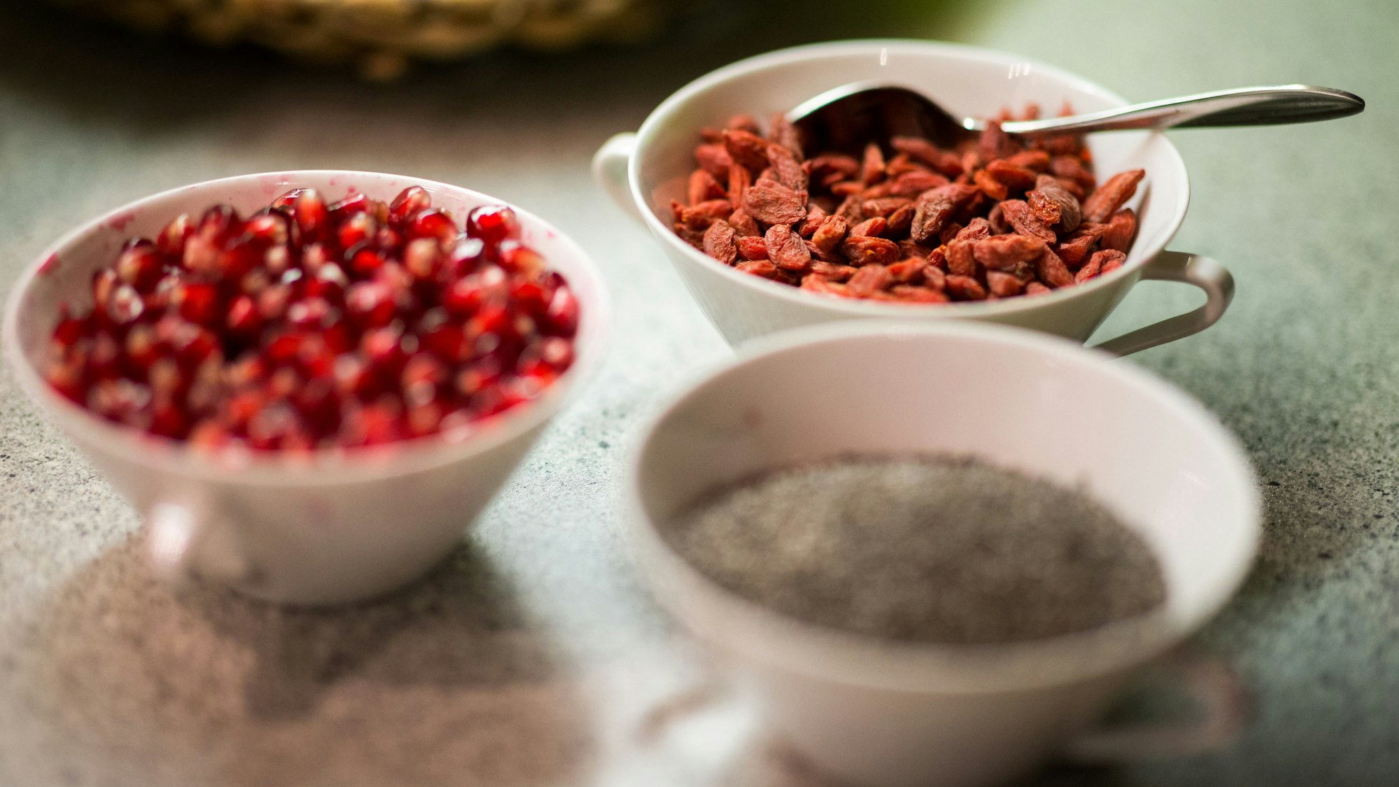Getrocknete Gojibeeren und Granatapfelkerne (l) stehen in Schüsseln auf einem Tisch.