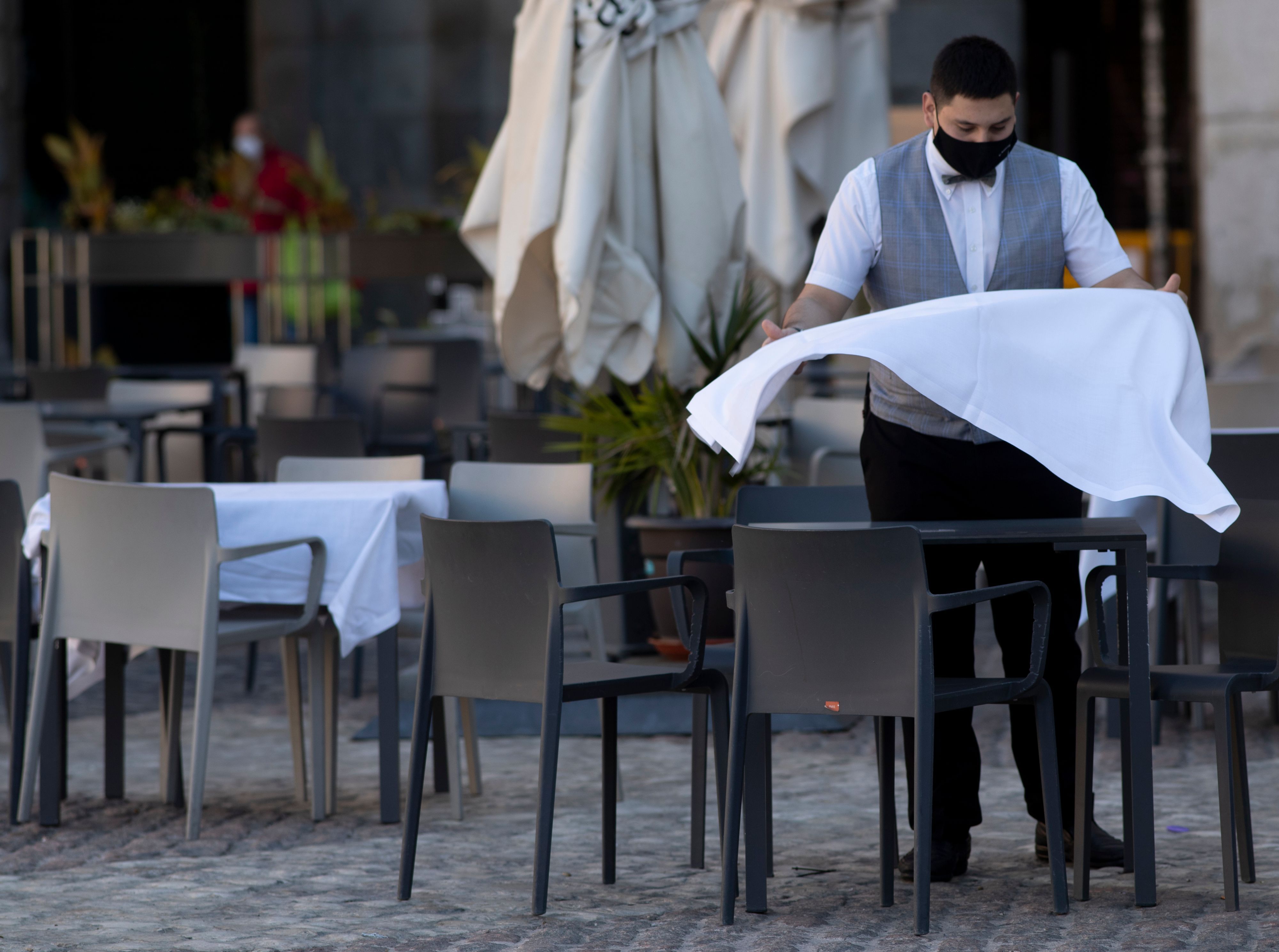 Ein Kellner mit Mund-Nasen-Schutz bereitet auf der Terrasse eines Restaurants einen Tisch vor.