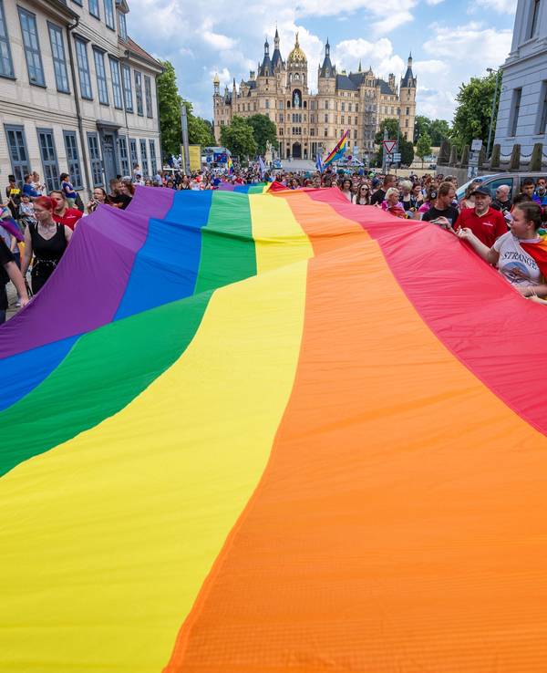 Mit einer großen Regenbogenfahne ziehen Teilnehmerinnen und Teilnehmer einer CSD-Parade in Berlin mit.