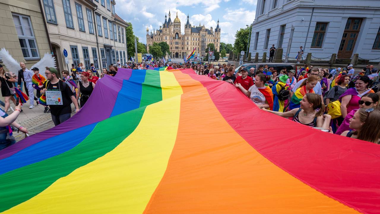 Mit einer großen Regenbogenfahne ziehen Teilnehmerinnen und Teilnehmer einer CSD-Parade in Berlin mit.