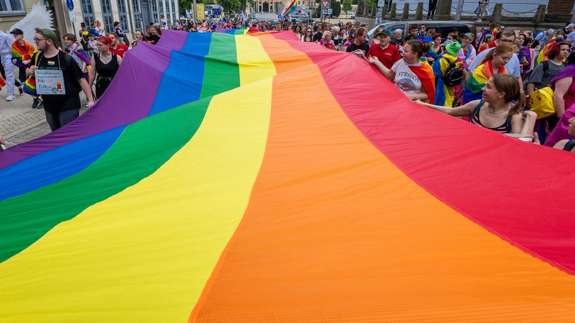 Mit einer großen Regenbogenfahne ziehen Teilnehmerinnen und Teilnehmer einer CSD-Parade in Berlin mit.
