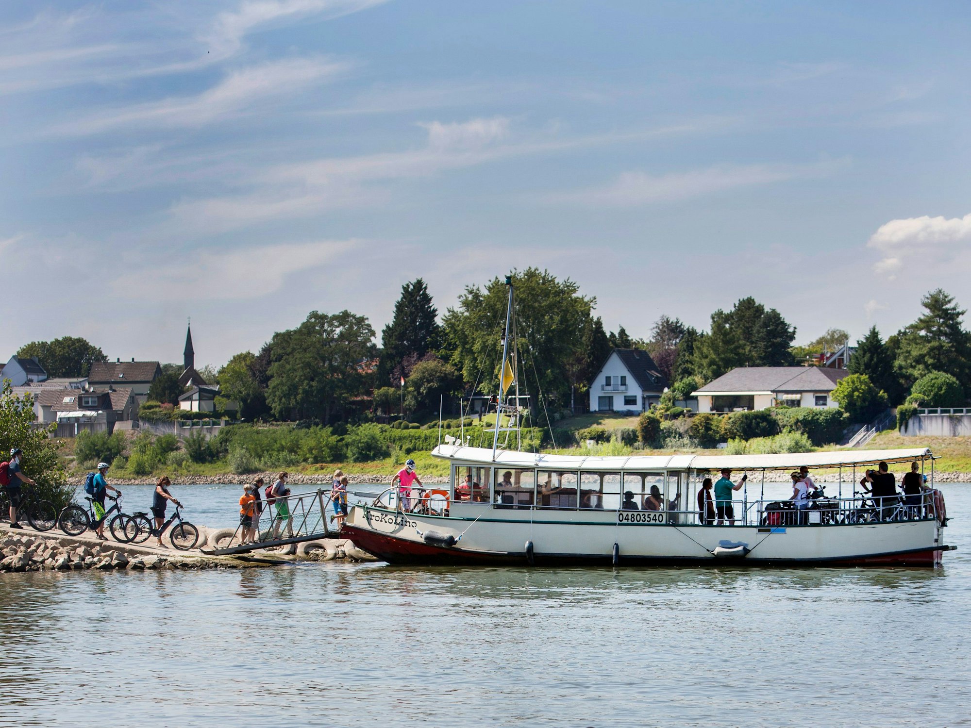 Fußgänger und Radfahrer steigen auf die Fähre Krokolino auf dem Rhein.