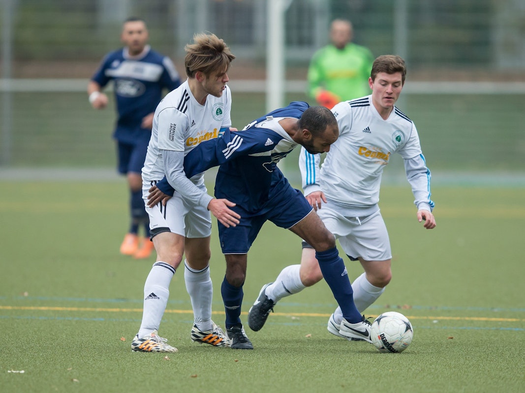 Drei Fußballer kämpfen bei einem Amateurspiel um den Ball.