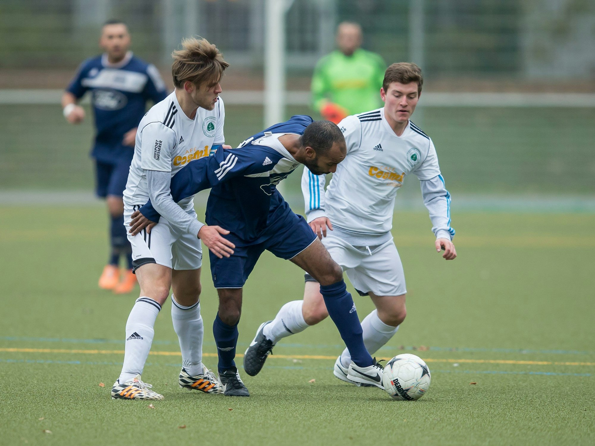 Drei Fußballer kämpfen bei einem Amateurspiel um den Ball.