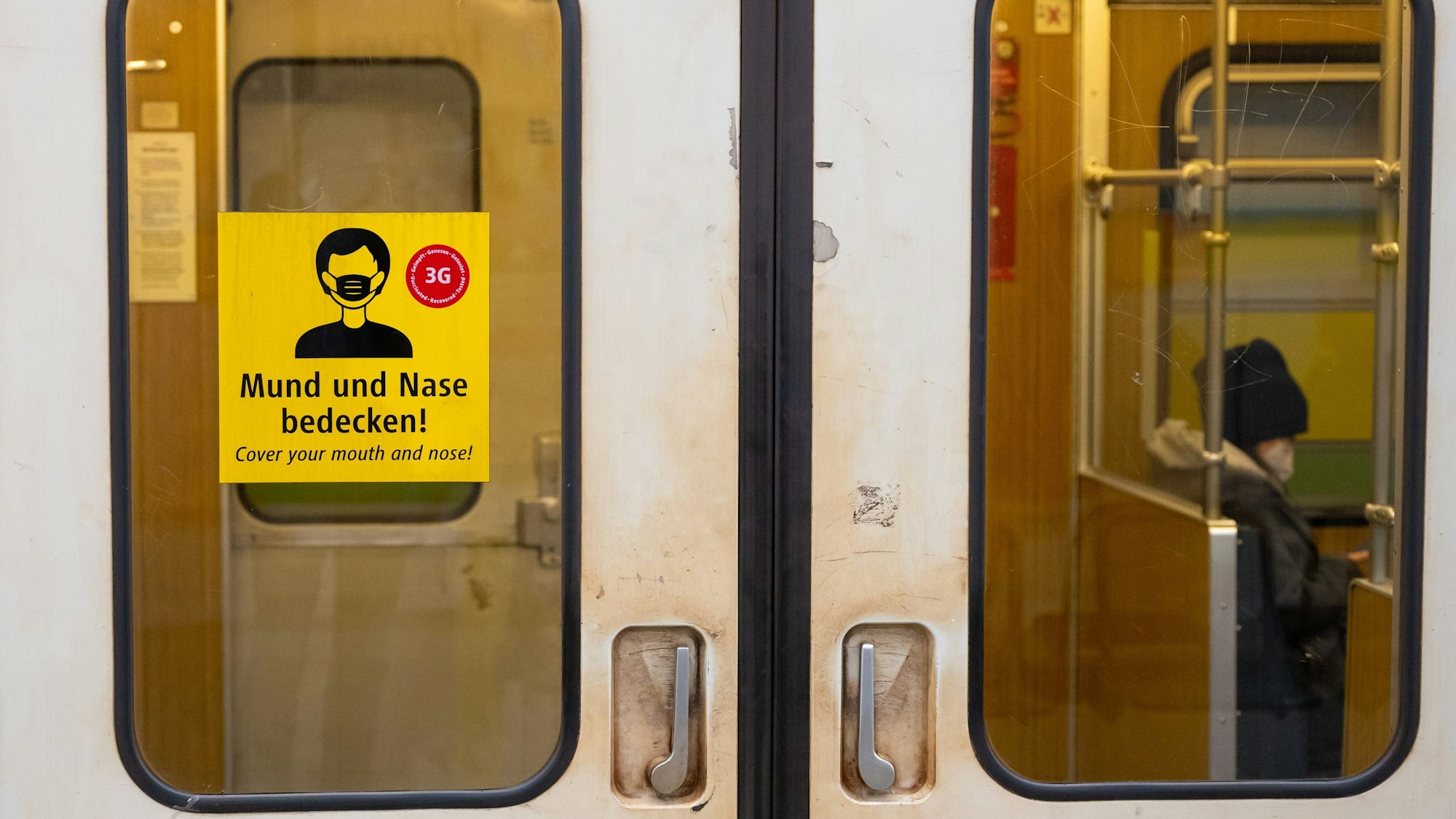 Ein Aufkleber mit der Aufschrift „Mund und Nase bedecken!“ ist an einer U-Bahn angebracht.