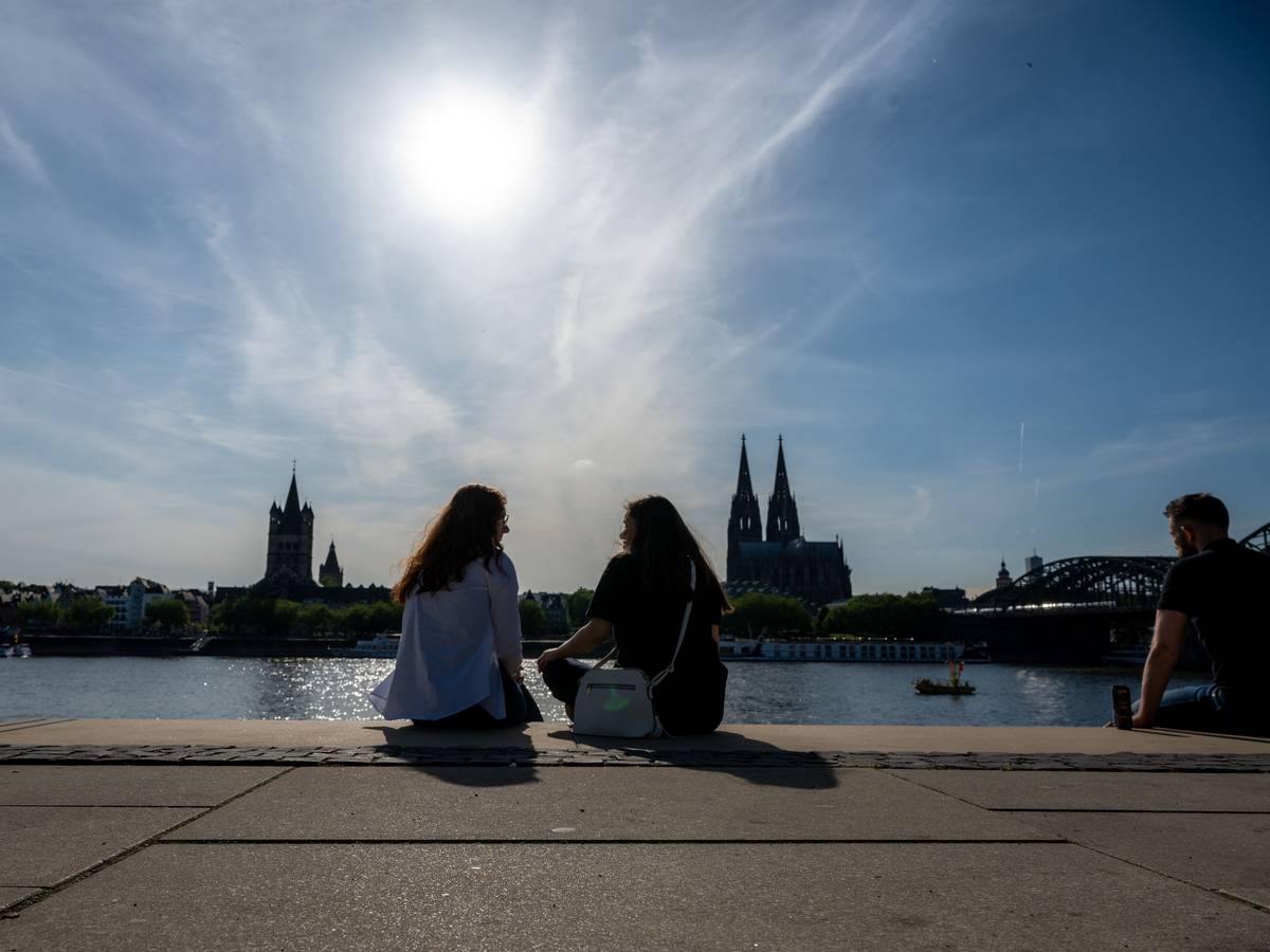 Zwei Frauen unterhalten sich am Rheinboulevard mit Blick zum Kölner Dom bei Sonnenschein.